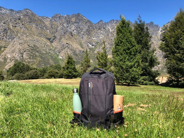 Backpack with dog treats and water bottle in grass by mountains in New Zealand.